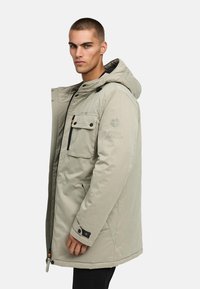 Kerged hall parka jakk kapuutsiga, millel on eesne lukuga sulgemine, mitmed taskud ja mustad aksessuaarid. Sujuv tekstuur ja kehakohane lõige.
