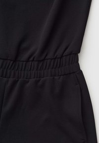 Black garment with elasticated waistband and side seam pocket, made of smooth fabric.