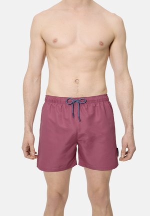 Modelo masculino vistiendo bañadores granate hasta la mitad del muslo con cordón azul, posando frente a un fondo claro y sencillo.