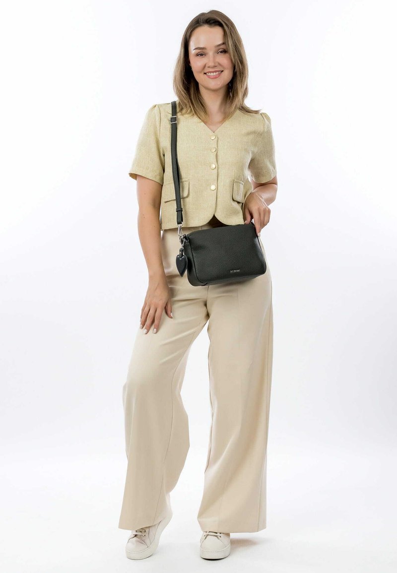 Lys beige kortærmet bluse med knapper, parret med løse cremefarvede bukser og hvide sneakers. En sort crossbody-taske med et hjertecharme.