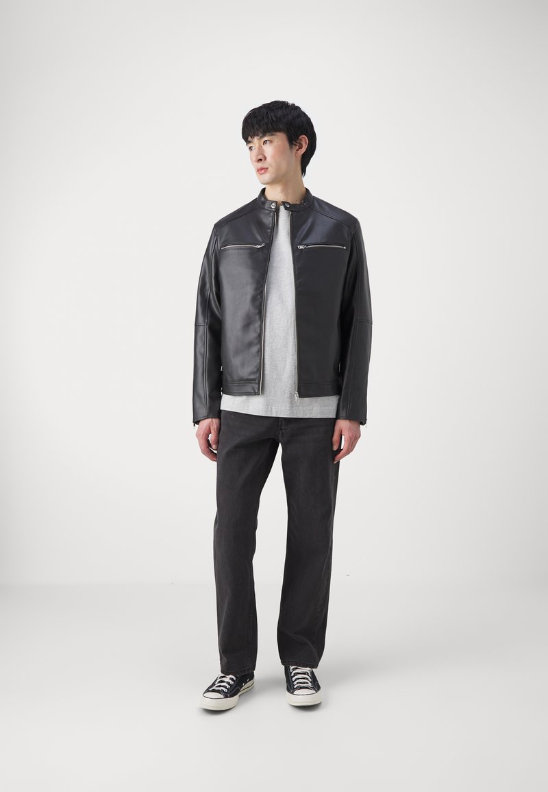 Schwarze Lederjacke mit Stehkragen, zwei vorderen Reißverschlusstaschen, kombiniert mit einem grauen Sweatshirt, dunklen Jeans und schwarzen Sneakern.