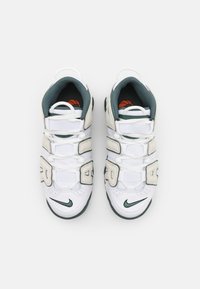 Sneakers atletiche bianche con dettagli verdi, dotate di tomaia in mesh e pelle, ammortizzazione sagomata e lacci spessi, etichettate con lettere in grassetto.