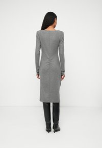 Vestido cinza de mangas longas com uma silhueta ajustada, detalhe de franzido nas costas e uma bainha reta. Combinado com botas pretas até ao joelho.