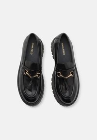 Mustadast nahast loafers, millel on dekoratiivne kuldne kett ja tuss, tekstureeritud sisetald ning paks ja vastupidav välistald.