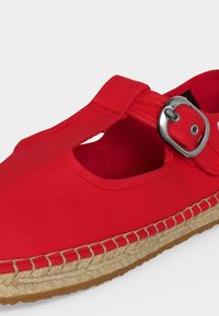 Κόκκινο καμβά Mary Jane παπούτσι με ασημένια αγκράφα, πλεκτή σόλα espadrille από γιούτα και καουτσούκ πάτο, εμφανίζεται πάνω σε απλό ανοιχτό φόντο.