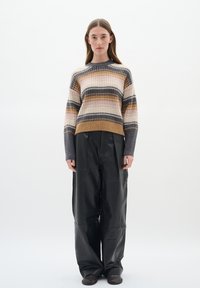 Strickpullover mit mehrfarbigen horizontalen Streifen in Beige, Grau und Braun; kombiniert mit lockeren schwarzen Lederhosen und flachen Schuhen.