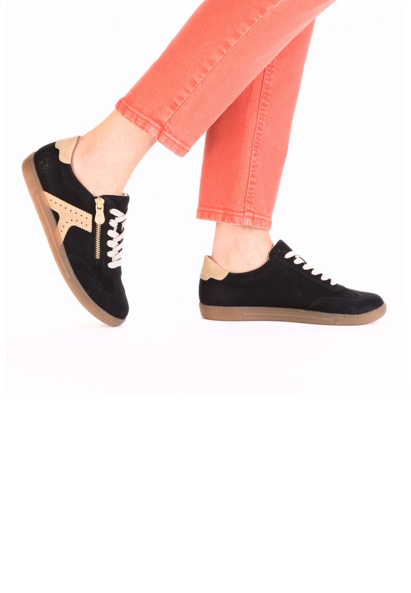 Black suede sneakers with beige accents, white laces, and a side zipper detail. Rubber sole. Worn with coral slim-fit jeans.