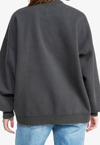 Sudadera XL de color gris oscuro con cuello y puños acanalados. Textura suave, corte relajado y sin patrones visibles ni detalles de hardware.