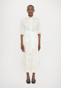 White linen dress with yellow floral embroidery, collared neckline, and three-quarter sleeves, tied at the waist with a matching belt.