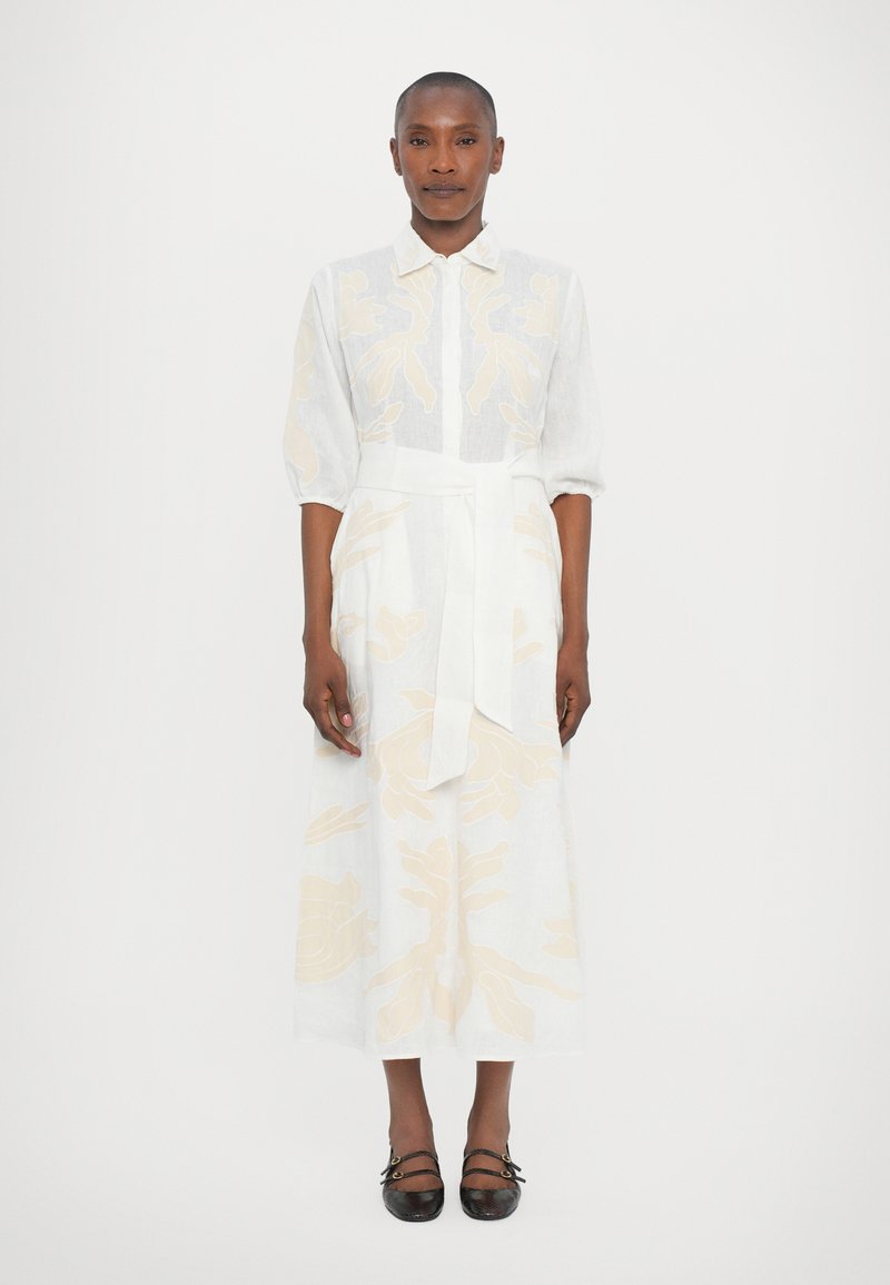White linen dress with yellow floral embroidery, collared neckline, and three-quarter sleeves, tied at the waist with a matching belt.