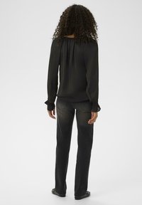 Blusa nera a maniche lunghe con cucitura arricciata sul retro, abbinata a jeans dritti grigio scuro, entrambi con una texture liscia e un design semplice.