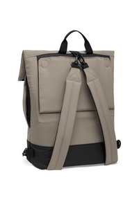 Batoh s mäkkým béžovým exteriérom, vybavený nastaviteľnými sivými popruhmi, uzáverom na klopu a čiernym spodným panelom. Obsahuje hornú rukoväť a kovové akcenty.