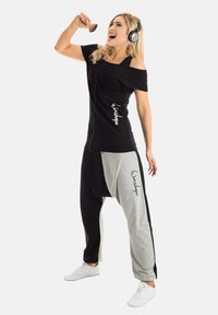 Black off-shoulder top and gray-black jogger pants with loose fit. The outfit features a logo print and a blend of textures.