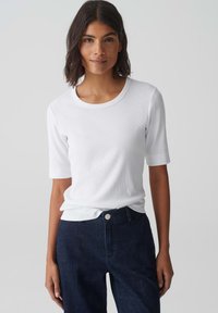 T-shirt bianco a righe con maniche corte e scollo rotondo, abbinato a jeans in denim blu scuro con chiusura a bottone.