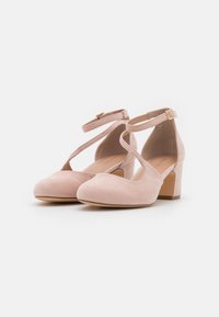 Scarpe con tacco in suede rosa con punta arrotondata, cinturini incrociati alla caviglia e tacco a blocco. Texture liscia con dettagli minimi.