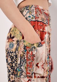 Pantalones de patchwork multicolores con cinturilla elástica, que presentan patrones florales y geométricos. Bolsillo lateral con detalles de ribete a juego.
