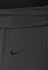 Pantaloni sportivi Nike in tessuto grigio scuro con una texture liscia; presentano un logo nero sul lato sinistro e una vita elasticizzata.