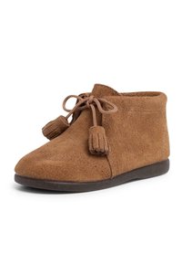 Botas de ante marrones hasta el tobillo con una suela plana, punta redonda y cordones atados con acentos de borlas. Textura suave con una suela más oscura que contrasta.