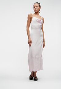 Φως ροζ σατέν φόρεμα με λαιμόκοψη cowl, λεπτά λουράκια και κομψή, εφαρμοστή σιλουέτα που φτάνει μέχρι το μέσο της κνήμης. Μαύρες κομψές γόβες.