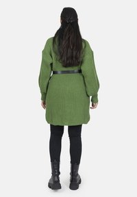 Cárdigan verde de punto con un ajuste holgado, mangas amplias y un cinturón negro en la cintura. Combinado con leggings negros y botas negras gruesas.