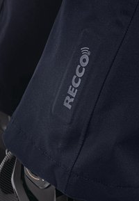 Námořnická voděodolná látka se hladkým povrchem; na nášivce je zobrazeno logo RECCO® se stříbrným písmem.