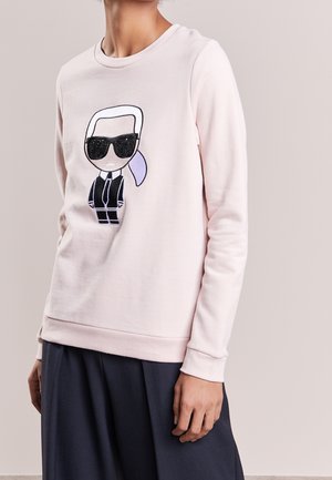 Jasnoróżowa bluza z nadrukiem kreskówkowej postaci o białych włosach, czarnych okularach przeciwsłonecznych, czarnej kurtce oraz lawendowym kucyku.
