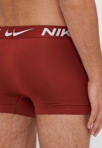Boxeri pentru bărbați dintr-un material roșu închis cu o textură netedă. Au o talie albă cu brandingul "NIKE".