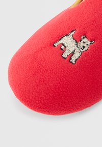 Chinelo de lã vermelha com um cão branco bordado na área do dedo do pé, apresentado sobre um fundo branco liso.