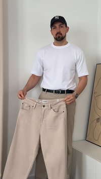 Beeži denimist teksapüksid, mida hoiab inimene, neil on viis taskut, metallkinnitused ja sirge lõige. Kantakse valget t-särki ja musta vööd.