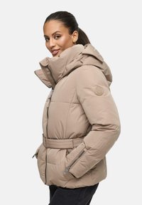 Beige pufferjack met een gequiltde textuur, hoge kraag, verstelbare riem en zijzakken; heeft een logopatch op de schouder.