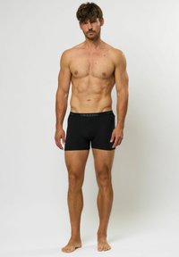 Boxeri negri dintr-un material moale, cu o croială ajustată. Prezintă un elastic cu logo-ul "Kappa" în gri. Modelul stă desculț.