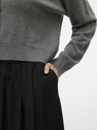 Maglione grigio lavorato a maglia con maniche lunghe abbinato a una gonna nera con tasche laterali e una trama liscia e fluida.