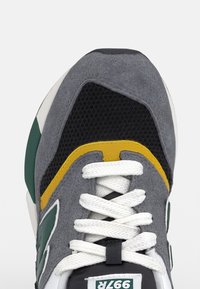 Šedé semišové tenisky s síťovanými detaily, zelenými a žlutými akcenty, bílými tkaničkami a klasickým robustním designem. Gumová podešev na spodní straně.