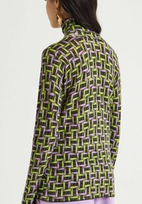 Maglia a maniche lunghe con collo alto realizzata in tessuto strutturato con motivo geometrico verde, lilla e nero. Collo alto e silhouette aderente.