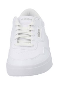 Vit sneaker med slät läderöverkropp, vadderad tunga, perforeringar på tåboxen, platta snören och en tjock vit gummisula. Logotyp på sidan.