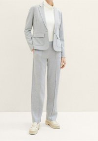 Lichtgrijs pak bestaande uit een op maat gemaakte blazer en broek met wijde pijpen, met een gladde textuur en subtiele stikdetails.