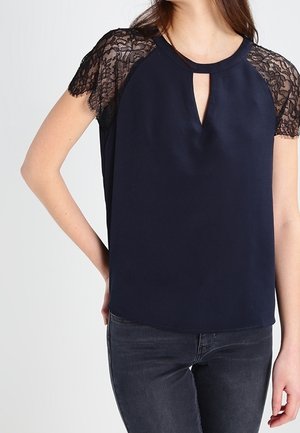 Haut marine avec des manches courtes en dentelle, décolleté en keyhole et coupe décontractée. Tissu doux avec un détail en dentelle texturée contrastée aux épaules.