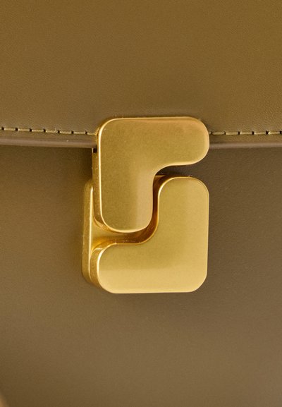 Χρυσό μεταλλικό κούμπωμα σε τσάντα χειρός ελιάς πράσινου χρώματος σε κοντινό πλάνο που δείχνει ραφές και λεία υφή.