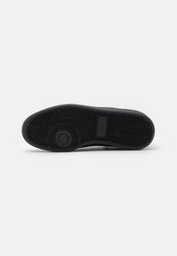 Black sneaker sole with textured herringbone pattern, circular emblem, and flat edge. Durable rubber material for traction and stability.