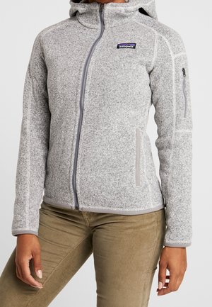 Light gray zip-up fleece jacket with hood, zippered chest pocket, and Patagonia logo on the upper left chest, worn with brown pants.
