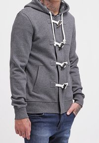 Grauer Kapuzenpullover mit vorderer Kordelzug-Verschluss, weißen Zugbindungen und Seitentaschen. Verfügt über eine weiche Textur und eine körpernahe Passform.