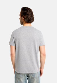 Sivé bavlnené tričko s krátkymi rukávmi, s okrúhlym výstrihom a rovnými okrajmi. Pohľad zozadu odhaľuje hladkú, mäkkú textúru. Bez grafiky alebo vzorov.