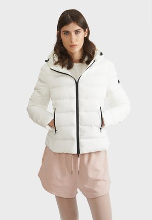 Veste en duvet blanche avec fermeture éclair sur le devant, accents noirs et capuche. Présente une texture matelassée et deux poches latérales pour un usage pratique supplémentaire.