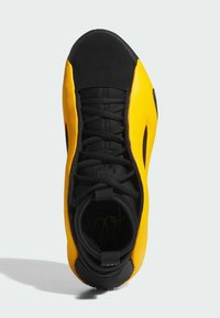 Geel en zwarte sportieve schoen met een getextureerde bovenkant, vetersluiting, rond teen en golvend zoolontwerp. Prominente branding aan de binnenkant.