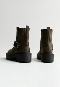 Bruna fusk läder ankelboots med en kraftig svart klack, dekorativ rem och spänne, dragkedjestängning och ribbat detaljer på ovansidan.