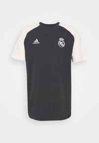 Camiseta Adidas en color azul marino con mangas cortas de raglán crema. Presenta un cuello redondo y el escudo bordado del Real Madrid en el lado izquierdo del pecho.