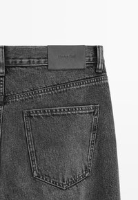 Czarne jeansy z denimu z skórzaną metką z napisem "Massimo Dutti", ciemnym przeszyciem oraz pojedynczą kieszenią o ostrym kształcie.