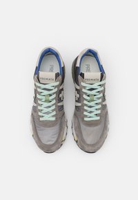 Pelēki tekstila sporta apavi ar zamšādas akcentiem, piparmētru krāsas šņorēm un zilu apkakli. Uz apaviem ir zīmola logo uz mēles un numuru detaļas uz zoles.