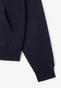 Navy sweatshirt featuring a textured cotton blend, a front pocket, and ribbed cuffs, emphasizing a wide, relaxed fit and durable stitching.