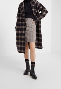 Abrigo de cuadros negro y marrón sobre una falda a rayas, combinado con botas de tacón negras y calcetines a rayas. Tela suave, diseño elegante.